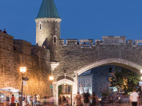 Par une chaude soirée d'été, des visiteurs se promènent sur la rue Saint-Jean, à proximité de la porte Saint-Jean.