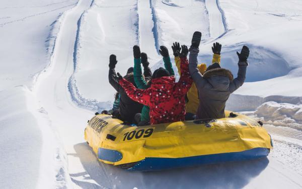 A group goes rafting on snow, arms in the air, in a slide at Village Vacances Valcartier.