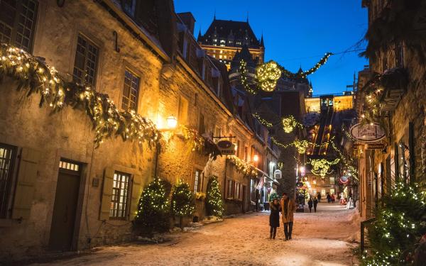 Un couple amoureux marche en soirée dans la rue du Petit-Champlain illuminée pour Noël et le temps des fêtes. 