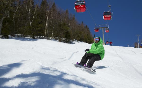 A snowboarder descends a slope at Mont-Sainte-Anne, below the cable car.