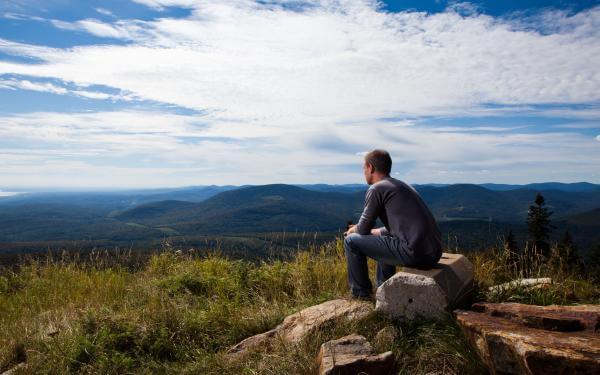 A man sits and observes the panorama on the La Crête trail at Mont-Sainte-Anne.