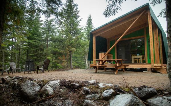 Vue extérieure d'un hébergement prêt-à-camper en forêt dans la Réserve faunique des Laurentides, en été.