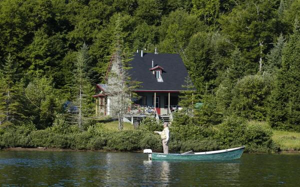 A house by the water and a fisherman in a rowboat in the Portneuf Wildlife Reserve.