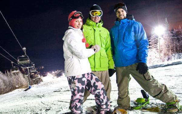 Three young snowboarders at Stoneham Ski Station in the evening.