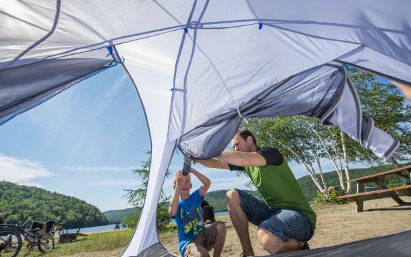 A father and his child set up a tent on a campsite near the water in the Portneuf Wildlife Reserve.