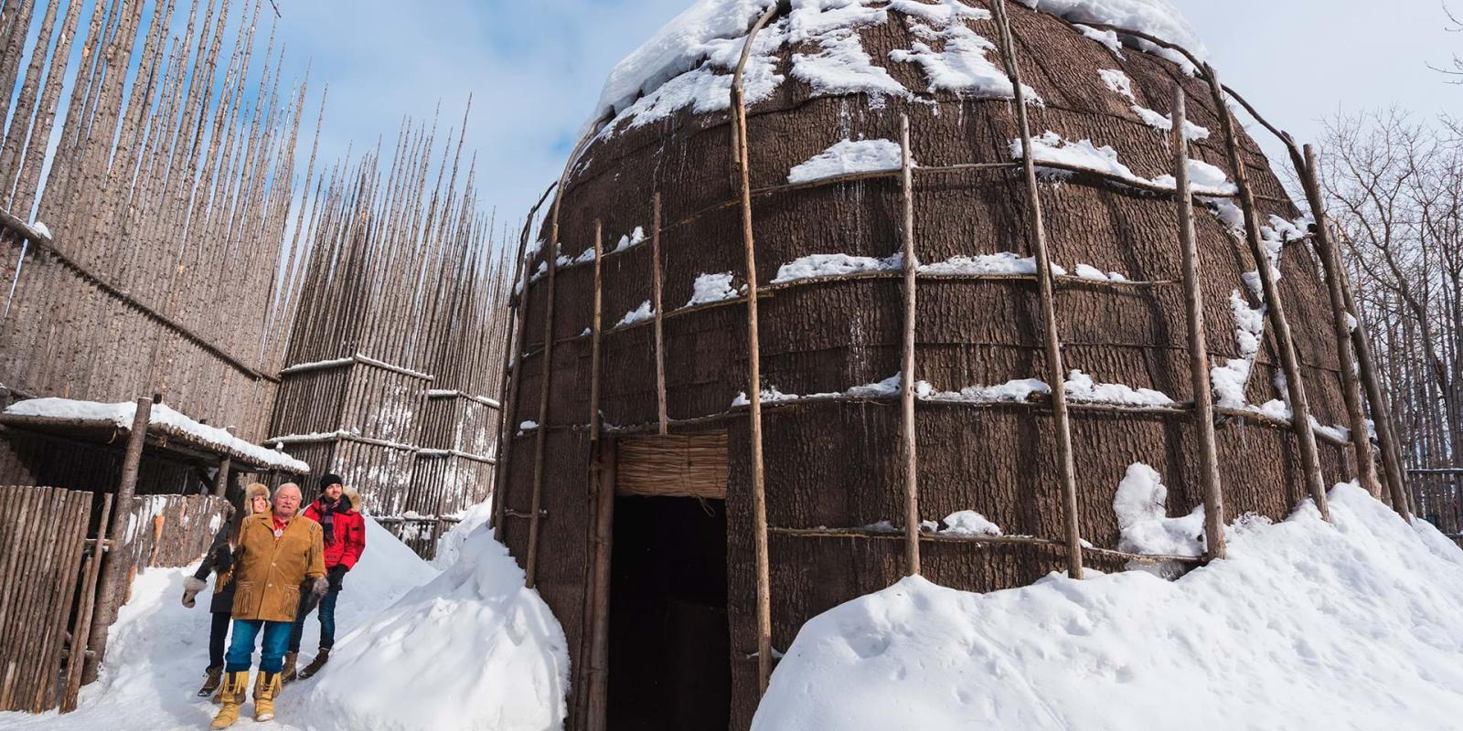 A couple walks outside the snowy longhouse with a guide, in Wendake near Québec City.