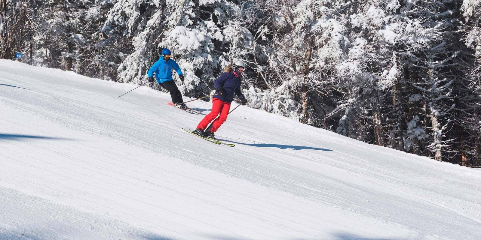 A man and a woman go downhill skiing at the Mont-Sainte-Anne resort.