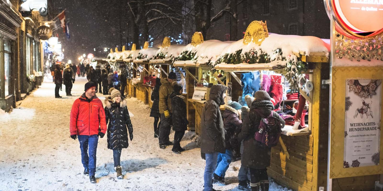 Plusieurs personnes marchent à l'extérieur et s'arrêtent aux nombreux kiosques du Marché de Noël allemand.