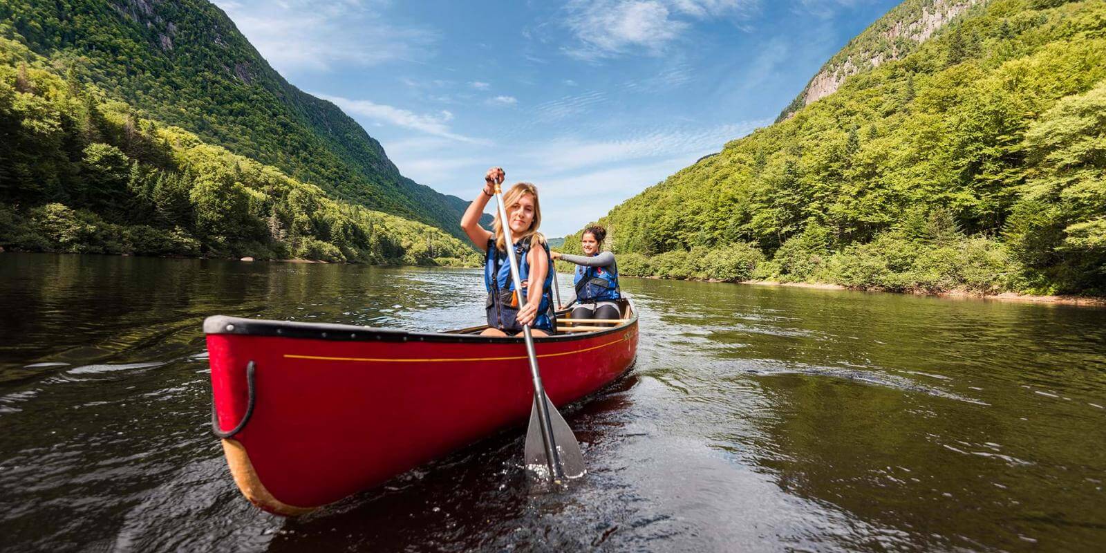 Two young women canoe in the river at the bottom of the valley, in Jacques-Cartier National Park.