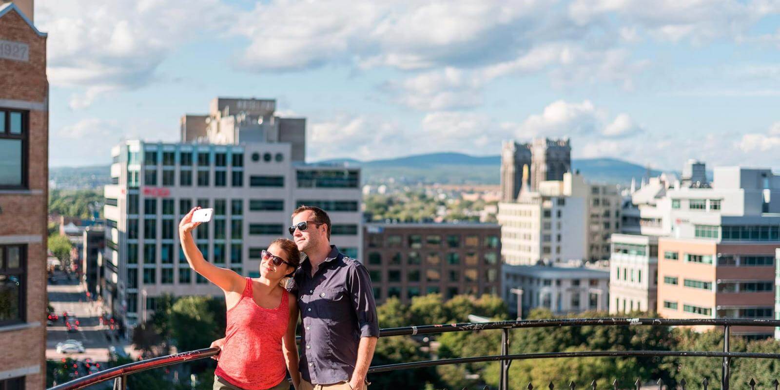 A couple takes a photo at the top of the Faubourg staircase with a view of the Saint-Roch district in the background.
