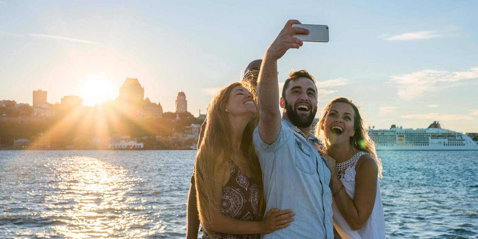 Friends take pictures of themselves at sunset, near the St.Lawrence River in Lévis with a panorama of Old Québec in the back.