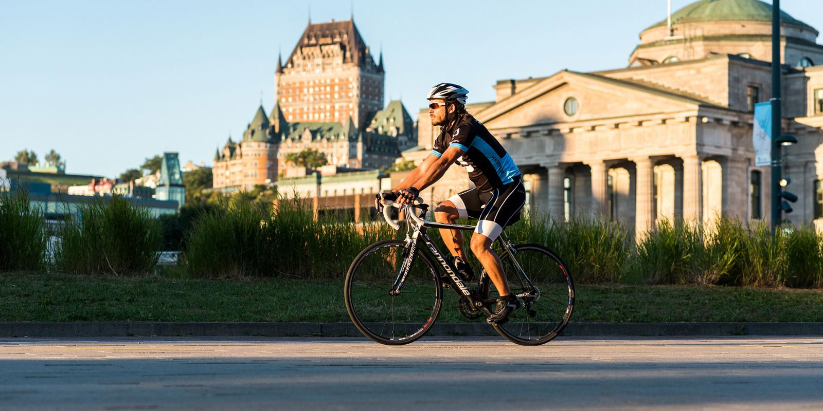 A cyclist rides on a bike path in the Old Port of Québec with the Château Frontenac in the background.