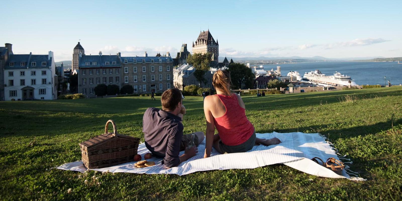 Couple picnicking near the Pierre-Dugua-De Mons terrace while admiring the Château Frontenac and the St. Lawrence River.