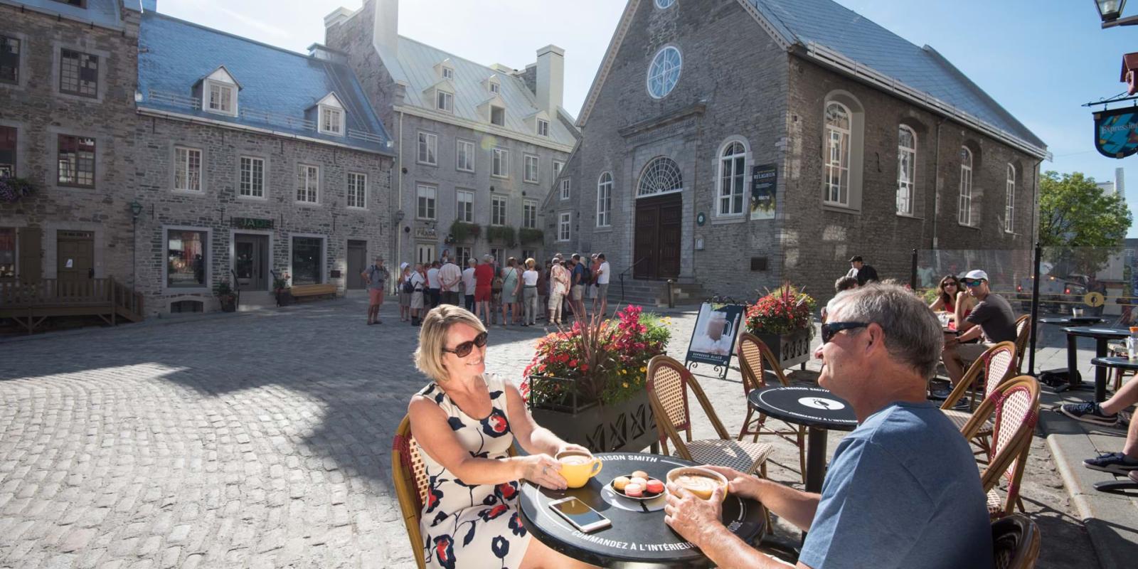 Un couple boit un café à côté de l'église Notre-Dame-des-Victoires, sur la terrasse de la Maison Smith à la place Royale.