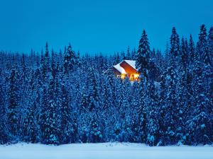 Vue extérieure d'un chalet illuminé au coeur d'une forêt enneigée, dans la Réserve faunique des Laurentides, en hiver.