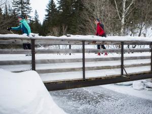 Deux personnes en ski de fond au Mont-Sainte-Anne, traversant un pont au dessus d'une rivière.