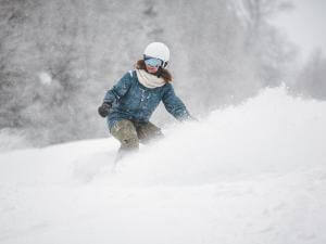 A woman is snowboarding in powder snow at Stoneham Ski Resort.