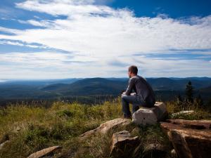 A man sits and observes the panorama on the La Crête trail at Mont-Sainte-Anne.