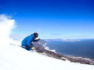 An alpine skier at the top of a mountain in the Massif de Charlevoix with a view of the St. Lawrence River.
