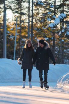 A couple skates on an icy skating trail in the forest.