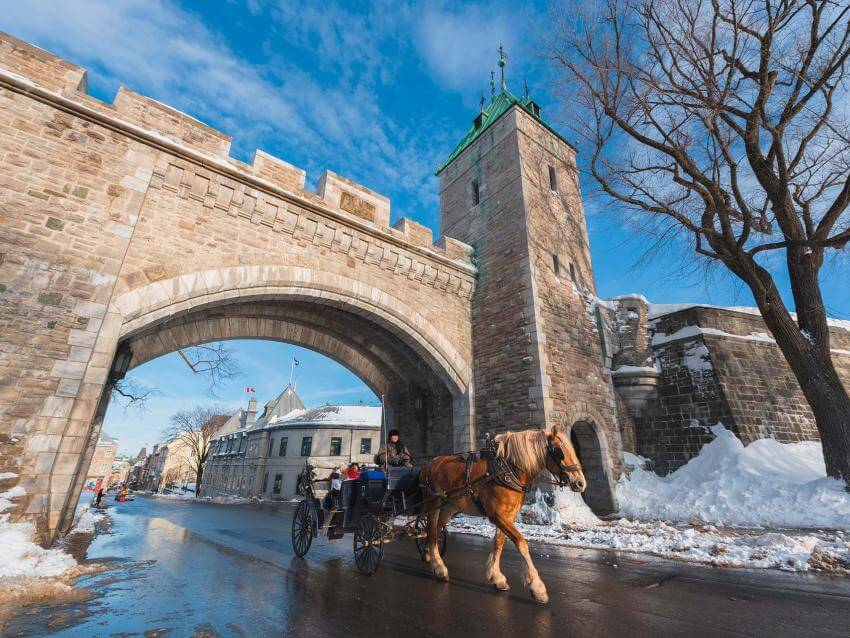Deux touristes en calèche passent sous la porte Saint-Louis en hiver.