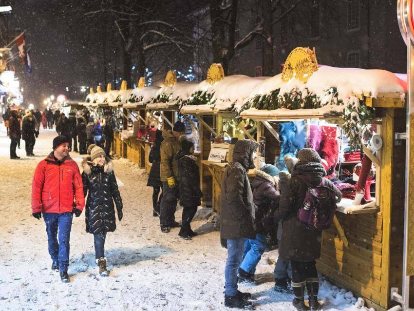 Several people walk outside and stop at the many kiosks at the German Christmas Market.