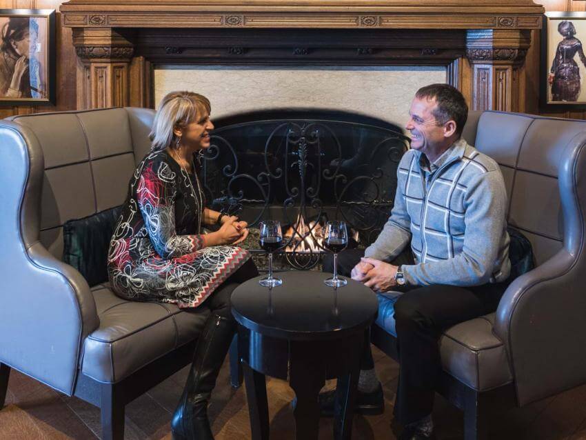 Un couple discute et boit du vin rouge au restaurant du Fairmont Le Château Frontenac, avec l'ambiance d'un feu de foyer. 