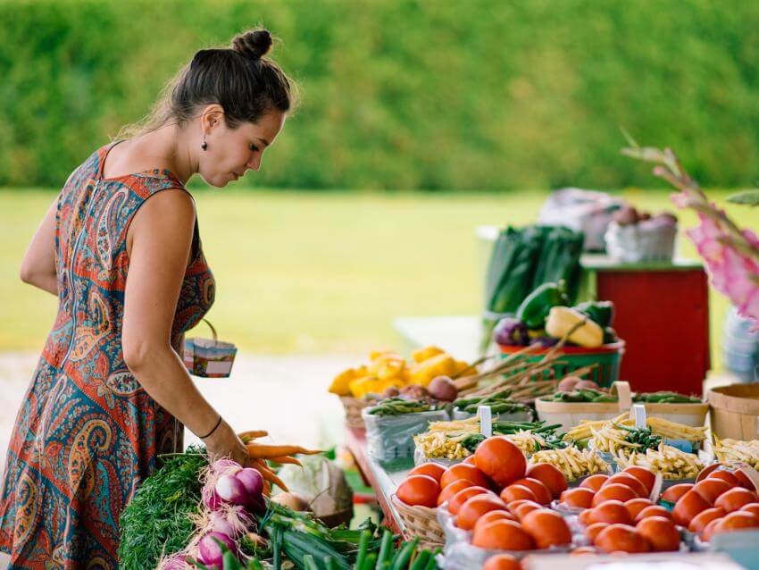 A woman buys fresh fruits and vegetables from an outdoor kiosk.