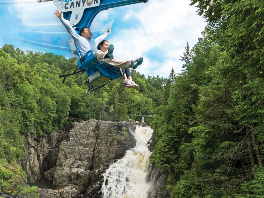 Two people cross the Sainte-Anne canyon, seated in the AirCanyon duo, near Québec City.
