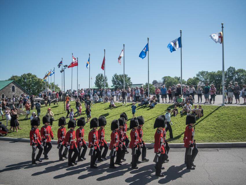 A crowd watches the changing of the guard with soldiers in red uniforms at La Citadelle in Québec in summer.