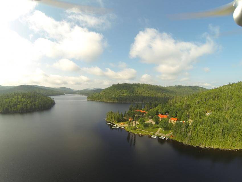 In the Réserve faunique des Laurentides, aerial view of the vastness of a lake in the middle of the forest and of several cabins with access to the lake, in summer.