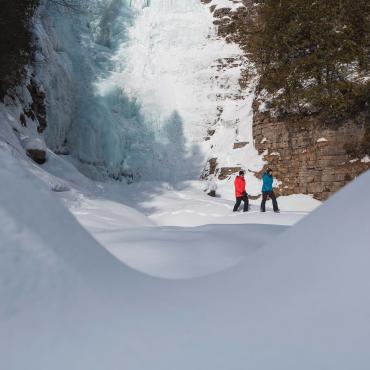 Two hikers walk in the snow at the foot of an icy waterfall, near Québec City.
