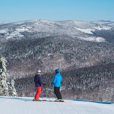 Deux skieurs observent les montagnes enneigées au sommet de la station de ski alpin du Mont-Sainte-Anne.