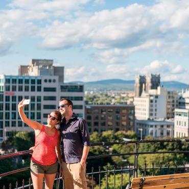A couple takes a photo at the top of the Faubourg staircase with a view of the Saint-Roch district in the background.
