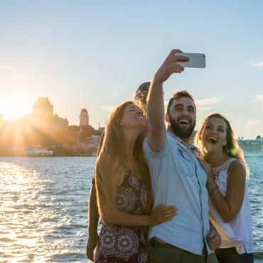 Friends taking a picture at sunset, near the St. Lawrence River in Lévis with a panorama of Old Québec in the background.