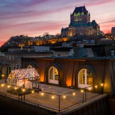 Couple qui mange dans une serre sous les étoiles sur le balcon d'une chambre de l'Auberge Saint-Antoine avec le Château Frontenac en toile de fond