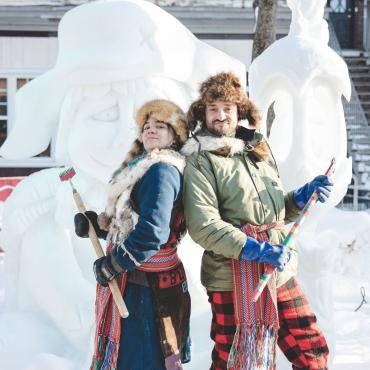 Deux personnages folkloriques devant une sculpture de neige au Carnaval de Québec