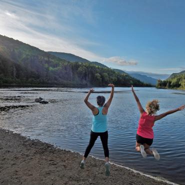 Deux filles sautent de joie devant la Vallée de la Jacques-Cartier, au Parc national de la Jacques-Cartier en été.