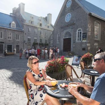 A couple drink a coffee next to Notre-Dame-des-Victoires Church, on the terrace of Maison Smith in Place Royale.