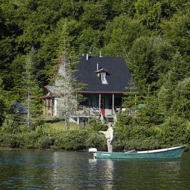 Une maison au bord de l'eau et un pêcheur dans une chaloupe dans la Réserve faunique de Portneuf.