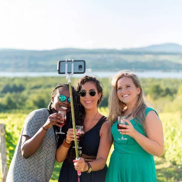 Three smiling girls take pictures of themselves and have a drink in the middle of a vineyard in Ile d'Orleans, in summer.